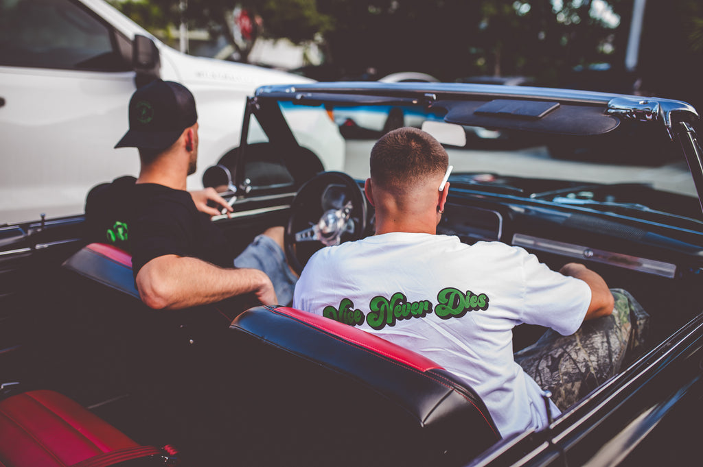 Doorcigs black snapback hat with logo, vice never dies tee and cigarettes in a classic car with black and red interior